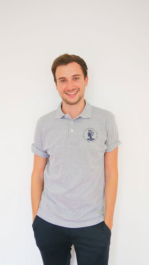 Eine junge Frau trägt das Polo-Shirt der BELS in blau. Ein junger Mann trägt das Polo-Shirt in grau melange. (öffnet Vergrößerung des Bildes)