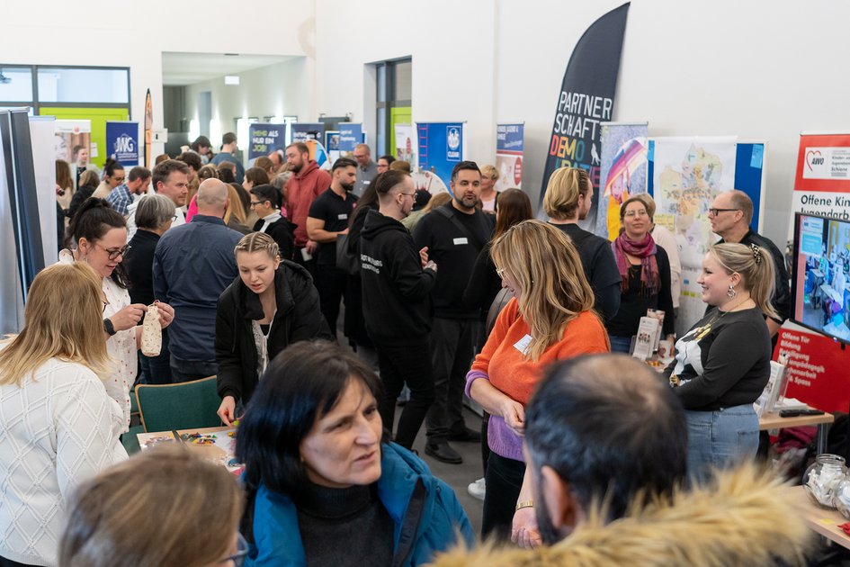 Ein Blick in einen Gang mit Ständen von verschiedenen sozialen Trägern, der gefüllt mit Besucher:innen ist.