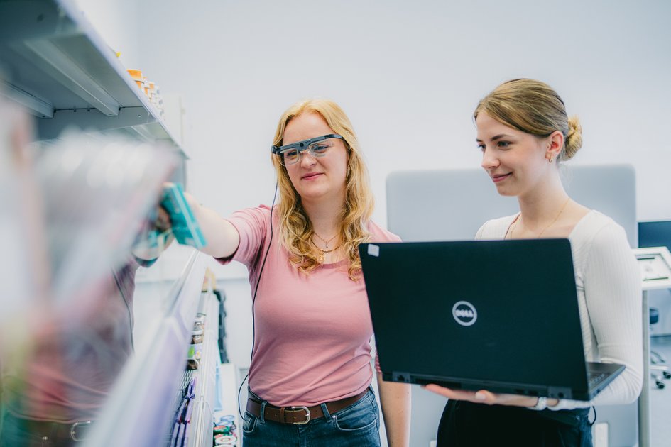 Zwei Frauen im Labor für experimentelle Markt- und Managementforschung analysieren Regalplatzierung, eine trägt eine Eye-Tracking-Brille, die andere hält einen Laptop.