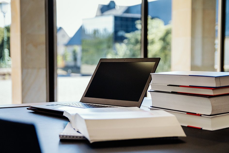 geöffneter Laptop mit einem Buch daneben liegend