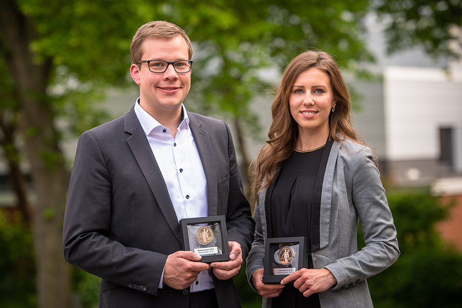 Die zwei ausgezeichneten Studierenden lächeln in die Kamera und halten ihre Awards in den Händen.