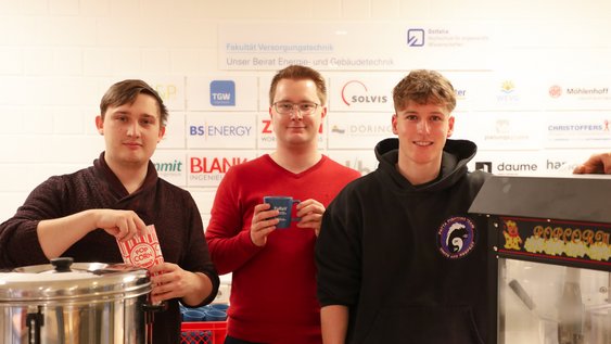 Drei Studierende des Fachschaftsrats bei der Aktion "Popcorn für die Studierenden" stehen nebeneinander und schauen in die Kamera.