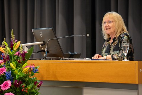 Die stellvertretende Bürgermeistermeisterin, Elke Wesche-Möller, bei ihrem Grußwort am Rednerpult, vor dem Pult ist ein Teil des Blumengestecks zu sehen. (öffnet Vergrößerung des Bildes)