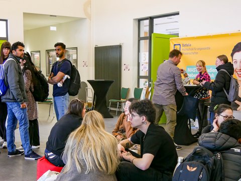 Im Foyer des Hörsaalgebäudes findet das Rahmenprogramm statt. Viele Personen informieren sich darüber oder sitzen entspannt auf den Sitzsäcken im Foyer. 