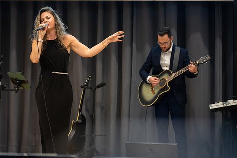 Das Musikduo Perceived as One, die Sängerin singt ins Mikrofon, ihr Partner im dunklen Anzug und mit weißem Hemd spielt Gitarre. (öffnet Vergrößerung des Bildes)