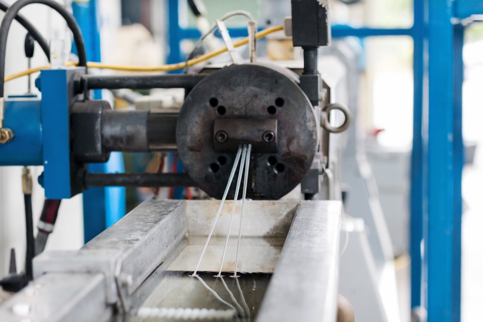 Eine Maschine spinnt dicke Fäden, die in ein kleines Flüssigkeitsbecken verlaufen