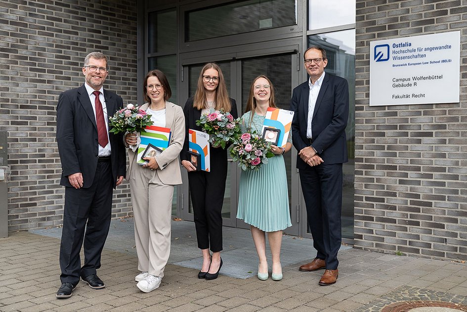 Drei Preisträgerinnen mit ihren Auszeichnungen und Blumensträußen in den Händen zusammen mit dem Dekan und Studiendekan vor dem Gebäude R.