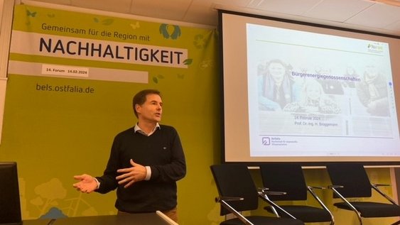 Prof. Dr.-Ing. Holger Brüggemann bei seinem Vortag über die Niedersächsische Lernfabrik für Ressourceneffizienz (NiFaR). Er steht am Rednerpult und gestikuliert mit seinen Händen. 