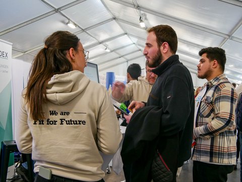 Info-Stand eines Unternehmens. Drei Personen sind im regen Austausch. 