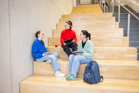 Studierende sitzen auf der Treppe im Gebäude G