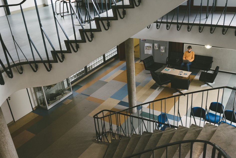Studierender arbeitet am Laptop an einer Sitzgruppe auf dem Flur zwischen Treppenauf- und -abgängen am Campus Wolfenbüttel.