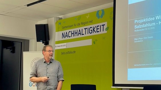 Dirk Staats steht am Rednerpult und hält seinen Vortrag beim Forum Nachhaltigkeit. Hinter ihm ist ein Teil seiner PowerPoint-Folie zu sehen.