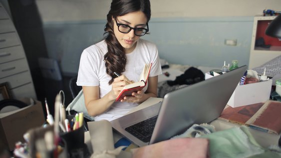 Eine Person am Schreibtisch schreibt in ihren Notizblock.