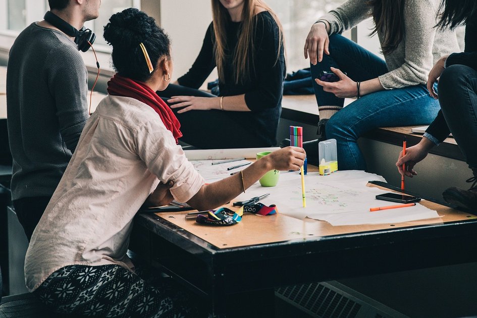 Decorative: Four young adults discuss and work together at a table with papers and pens, symbolising cooperation in the field of business administration and management.