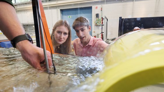 Zwei Studierende betrachten einen Versuchsaufbau in der Wellenrinne der Wasserbauversuchshalle am Campus Suderburg.