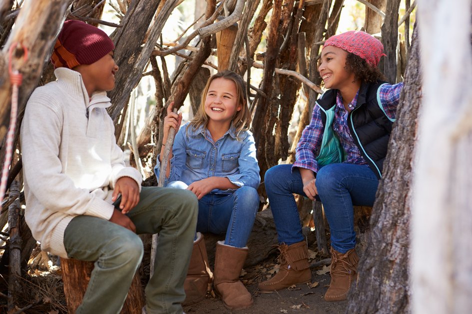 drei Kinder sitzen im Waldin einem Holz aus Stöcken