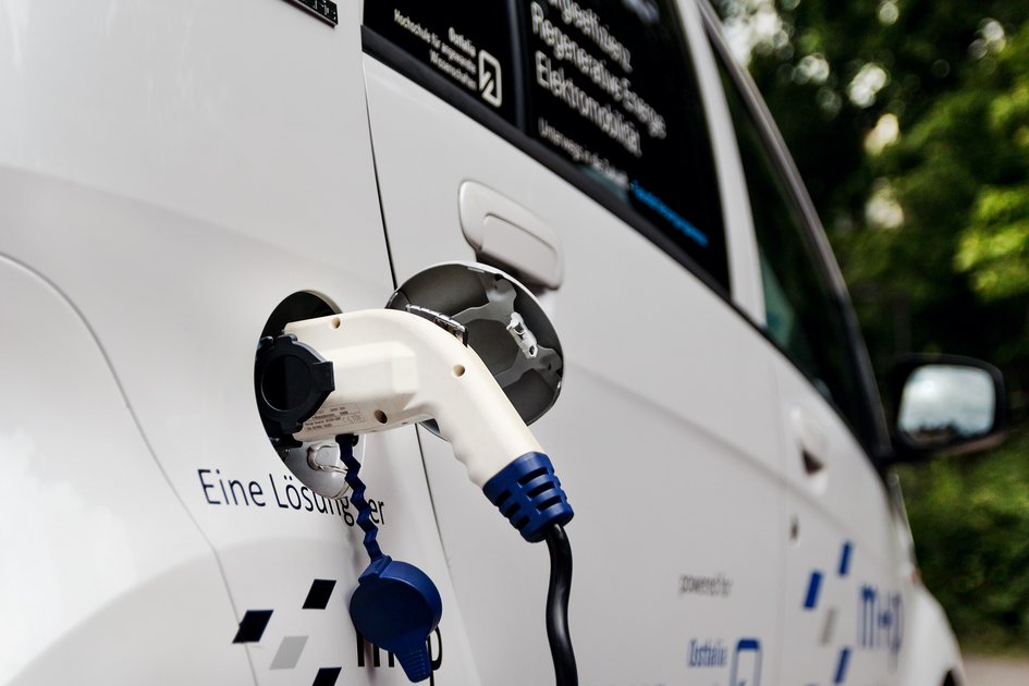 Tankdeckel eines Elektroautos, das im Grünen steht und über ein Kabel geladen wird