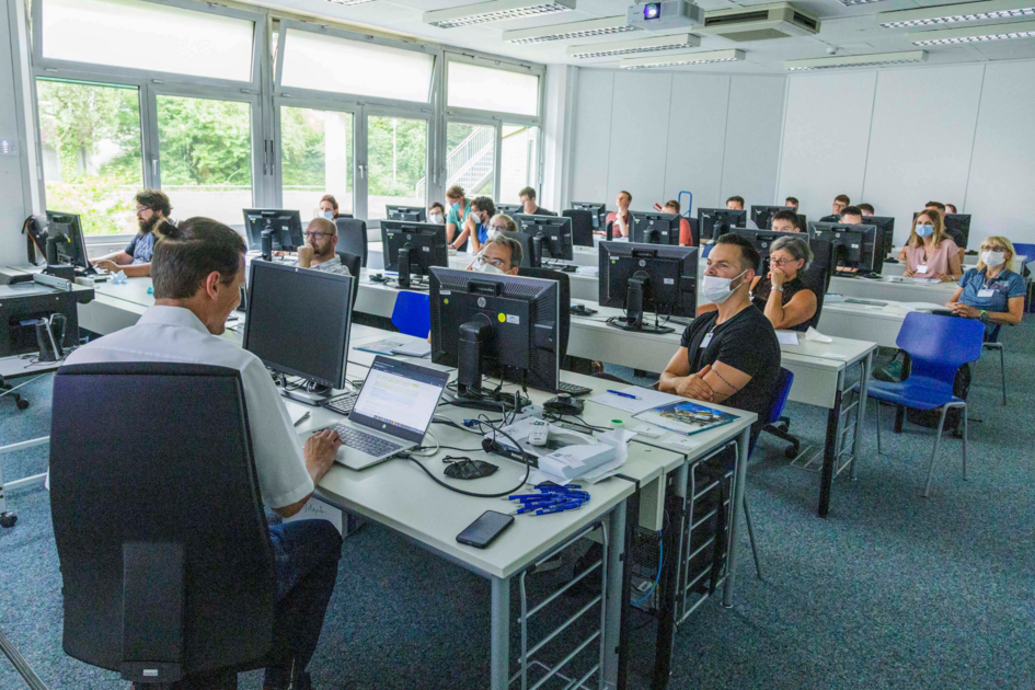 Blick in den Poolraum im Rechenzentrum, wo eine größere Gruppe an Menschen Richtung eine Beamerleinwand schaut