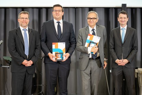 Prof. Dr. Kai Litschen zusammen mit den ausgezeichneten Lehrbeauftragten Nico Herrmann und Dr. Roland Wierling und Prof. Dr. Till Zech. Die Ausgezeichneten stehen in der Mitte und halten ihre silbernen Medaillen. (öffnet Vergrößerung des Bildes)