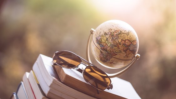 Kleiner Globus und Sonnenbrille auf einem Stapel Bücher