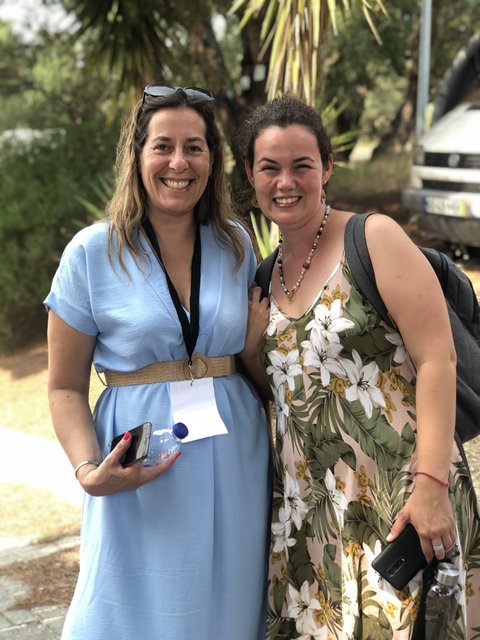 Two women pose in front of palm trees