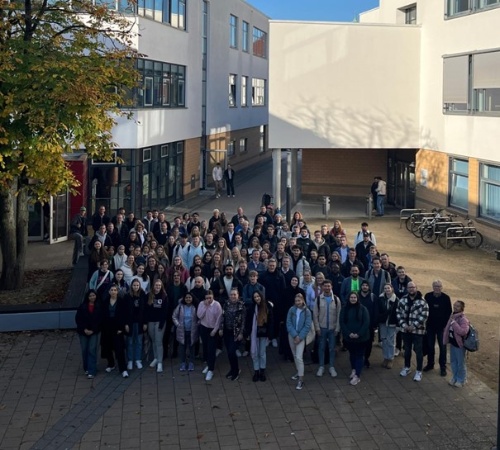 eine große Personengruppe steht zwischen Gebäuden. Das Foto wurde aus einer erhöhten Position geschossen.