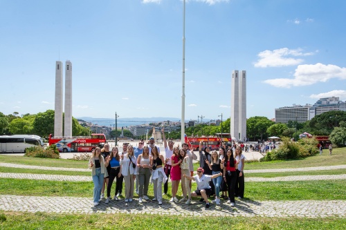 Personengruppe posiert auf einer Rasenfläche. Im Hintergrund ist die Stadt Lissabon zu erkennen
