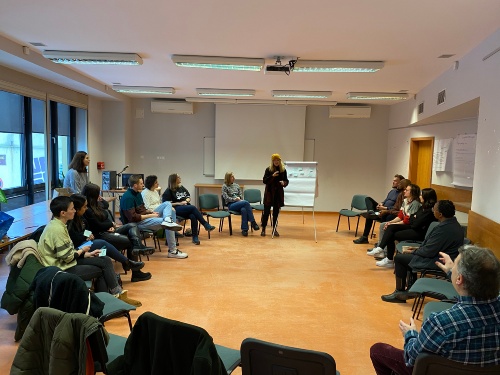 Personen sitzen in einem Stuhlkreis und hören einem Vortrag zu 