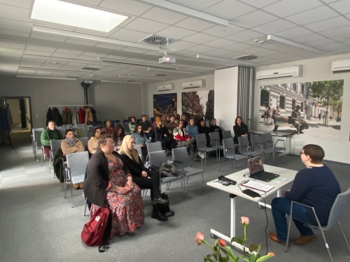 Personen sitzen in einem großen Büro- bzw. Seminarraum auf Stühlen und hören einem Vortrag zu